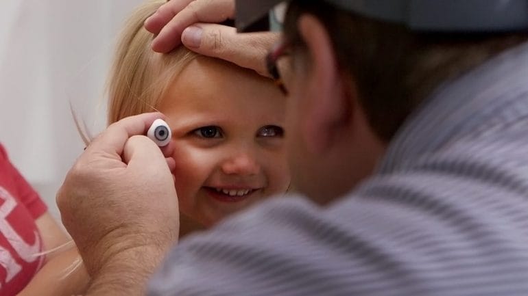 Ocularist fitting a young girl with a prosthetic eye