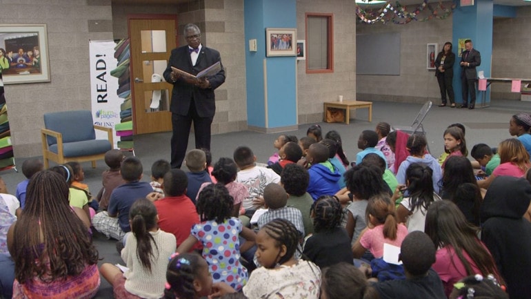 Kansas City, Missouri Mayor Sly James stands and reads in front of group of students sitting on the floor.