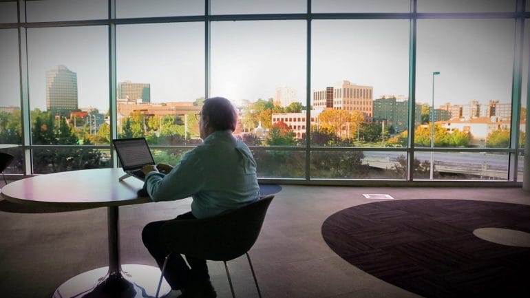 Image of man working on computer with mid-town Kansas City buildings outside large windows