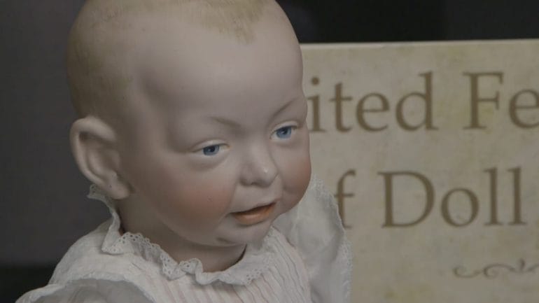 Close-up image of painted bisque baby doll in white linen gown.