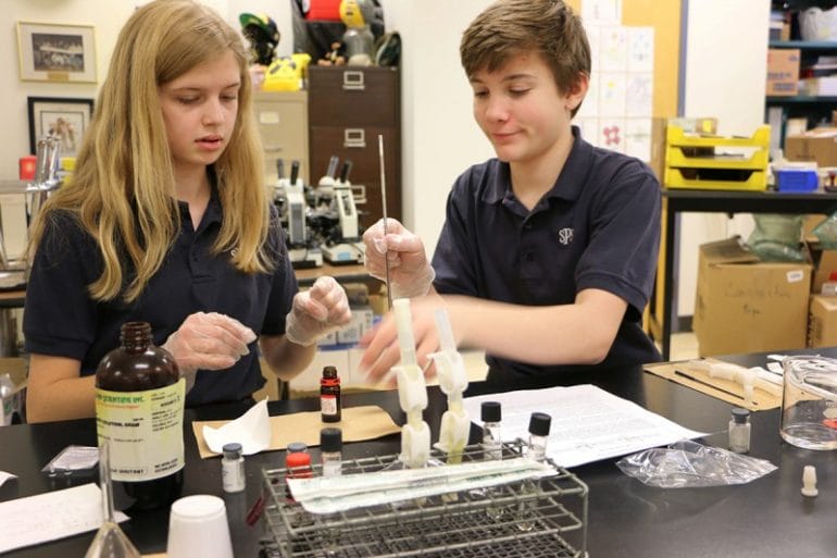 Photo of two students sitting at a table with lab equipment.