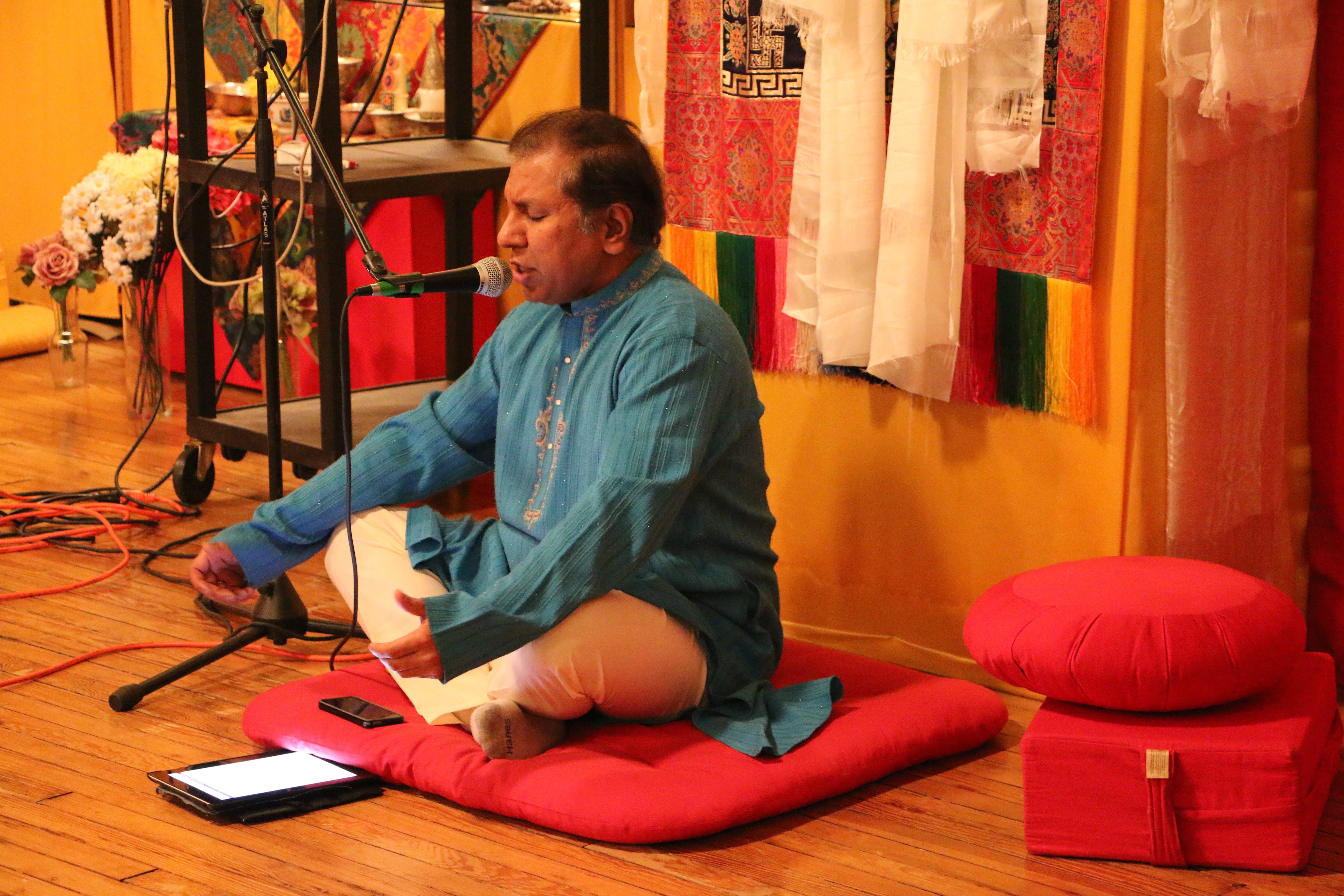 a man sits cross-legged on a cushion, eyes closed in prayer