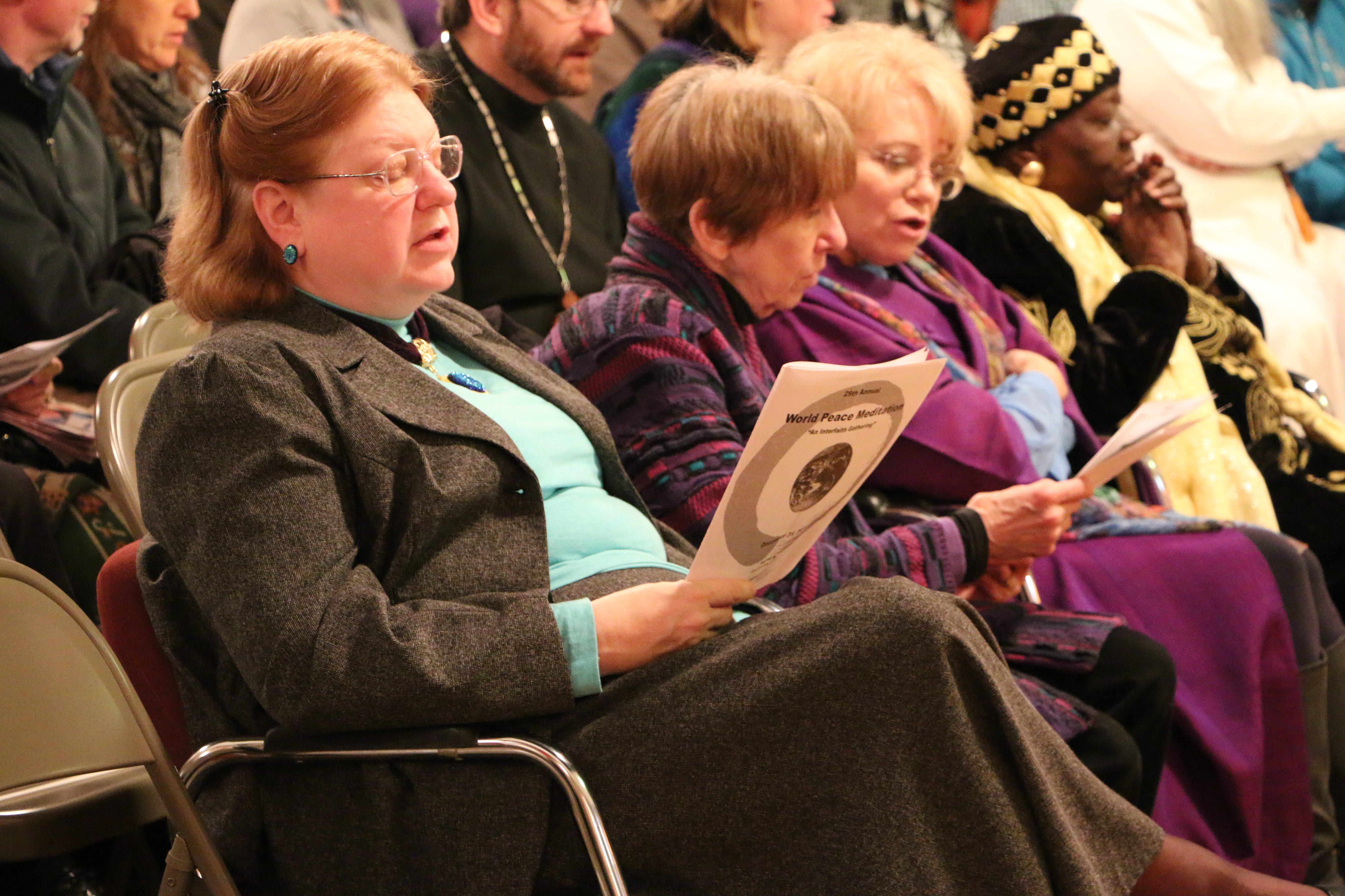 A woman sits, reading the back of the program