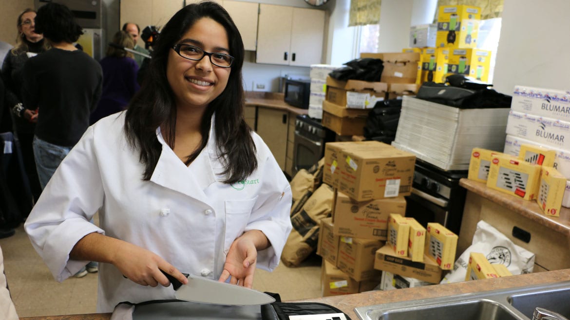 teen girl in white chef's coat poses wilth chef's knife.