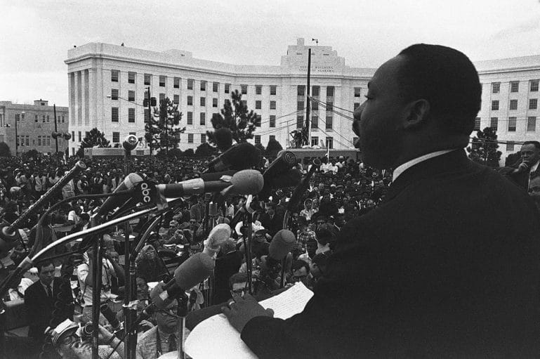 Black and white photo of MLK in front of large crowd.