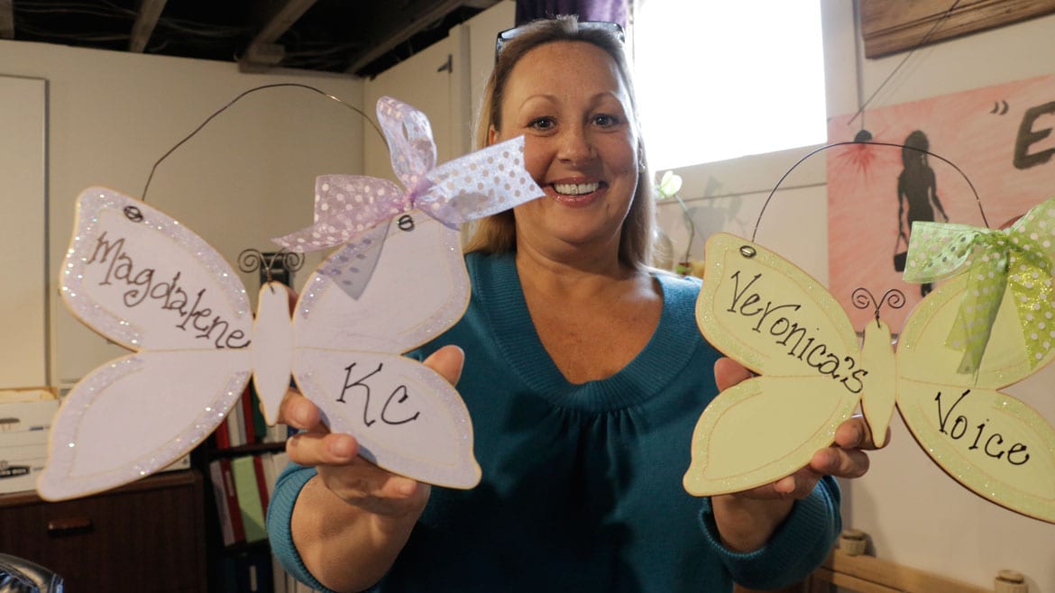 A woman in a blue sweater holds up two decorative butterflies. One says 