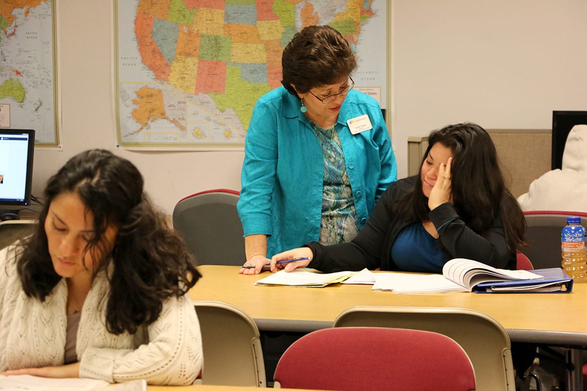 Image of woman standing next to woman seating at a desk.