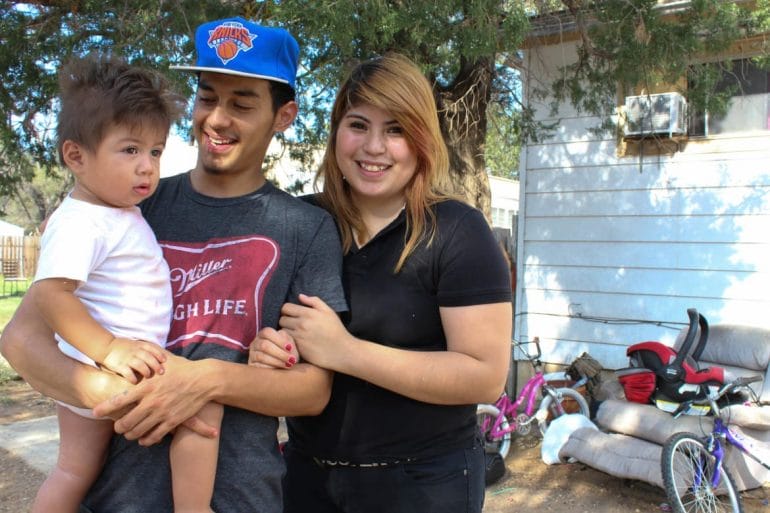 Claudia Rivera (right) and her boyfriend, Jesùs Varela, stand in the yard of their Liberal, Kansas, home with their 1-year-old son, Fabian. (Photo: Esther Honig | Heartland Health Monitor)