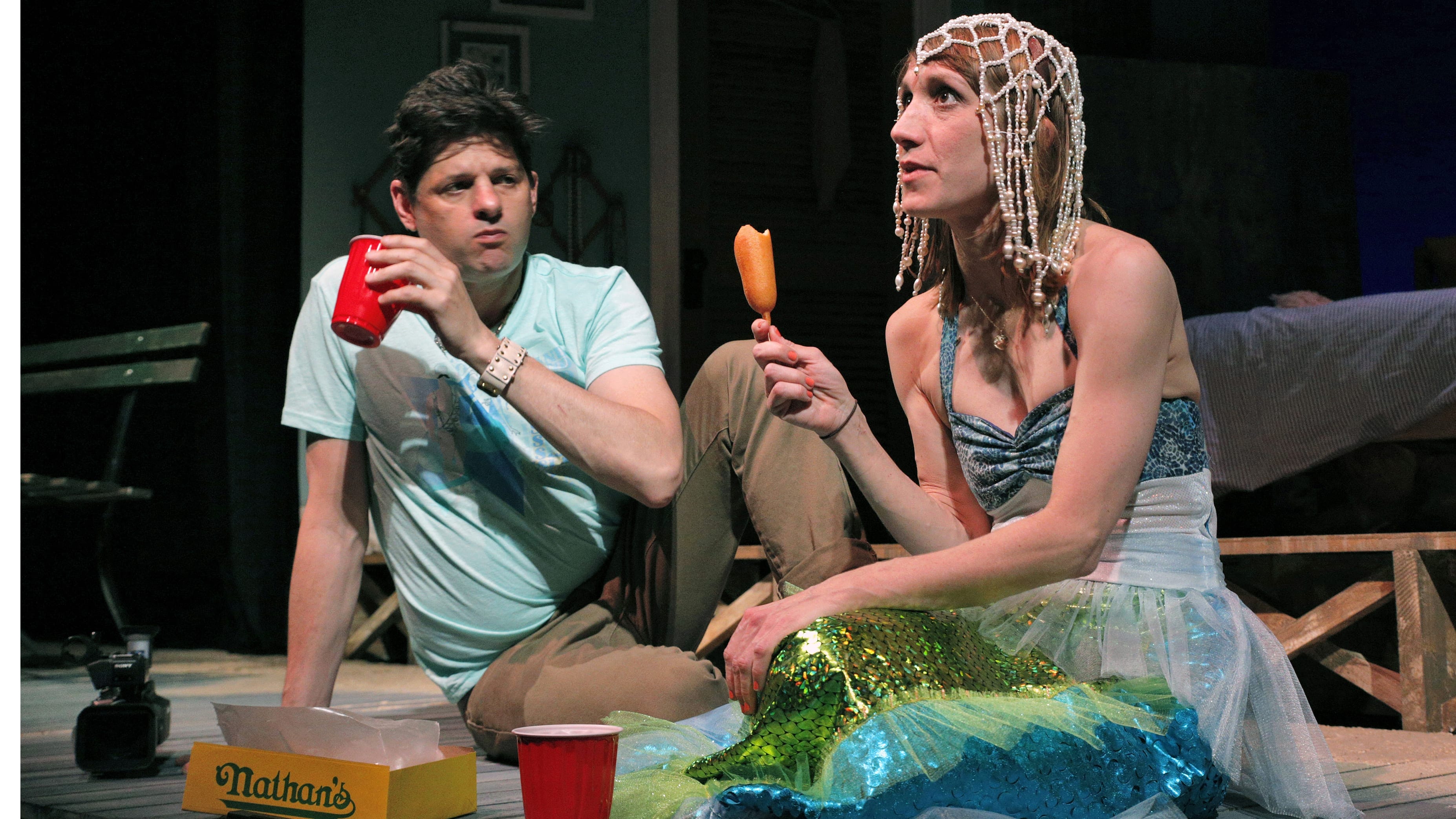 two actors on a stage, eating coney dogs