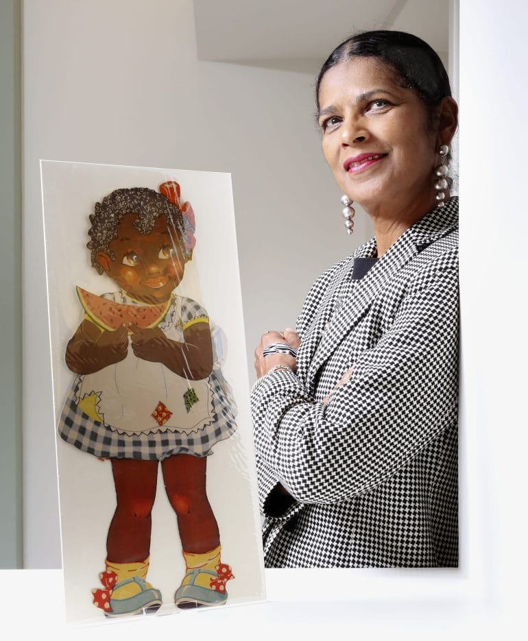 This photo shows Arabella Grayson standing next to her private collection of African American paper dolls.