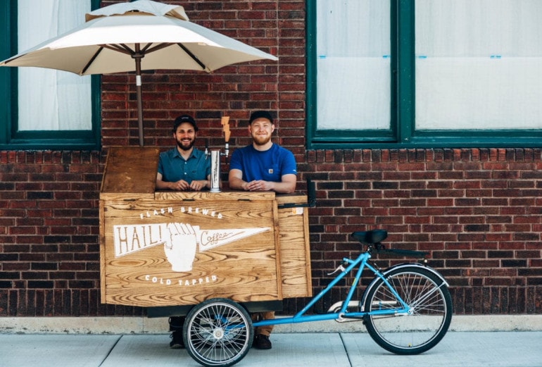 Two men stand behind their coffee cart.