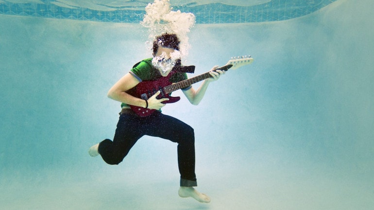 a teenager playing a guitar underwater