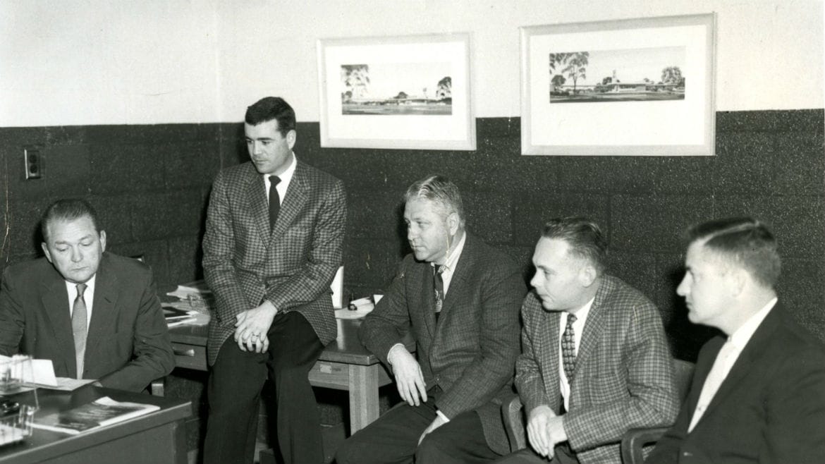 Five men in suits sitting around a desk.