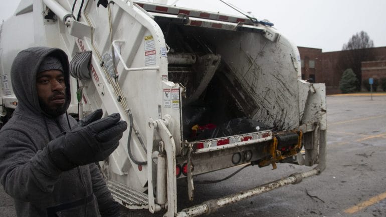 worker guiding motorist to trash truck