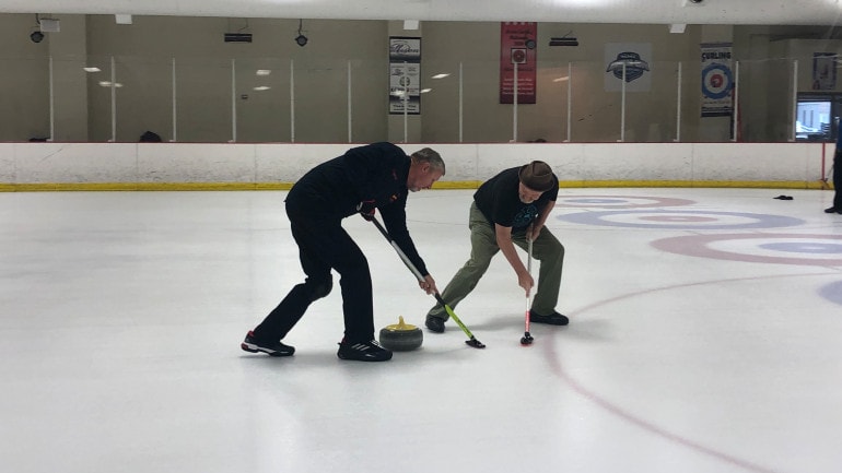 A pair of curlers sweep in front of the stone.