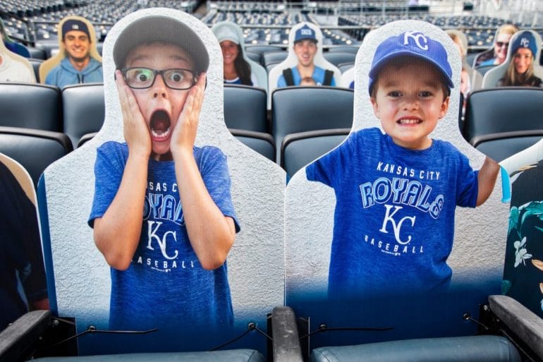 Two cardboard cutouts of fans resting in Kauffman Stadium's bleachers, ready for the home opener.