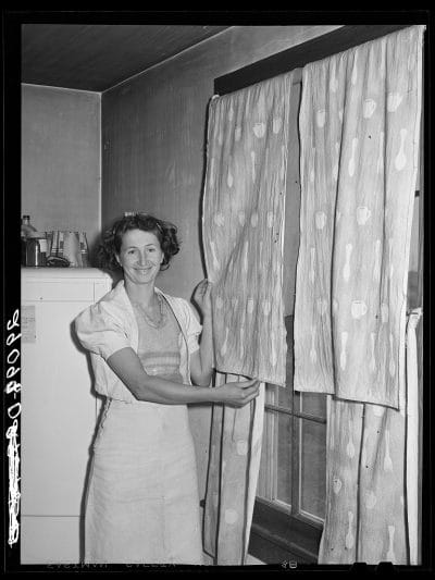 The FSA (Farm Security Administration) home supervisor helped this woman make her dress of flour sacks and decorate her curtain with splatter work in Osage Farms, Missouri, 1939.