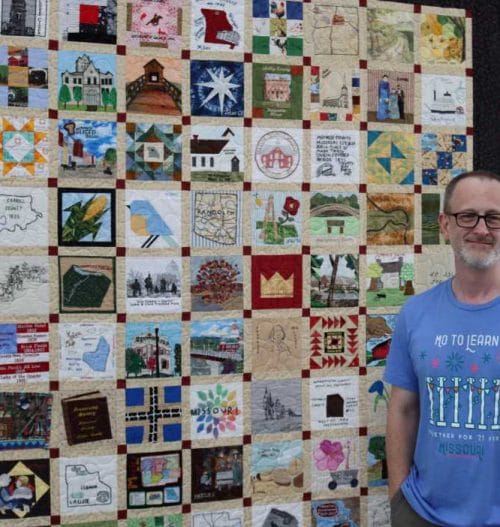 Michael Sweeney has driven the Missouri Bicentennial Quilt all around the state to make sure everyone can see it. Here he stands next to it at its exhibition in Columbia, Missouri.