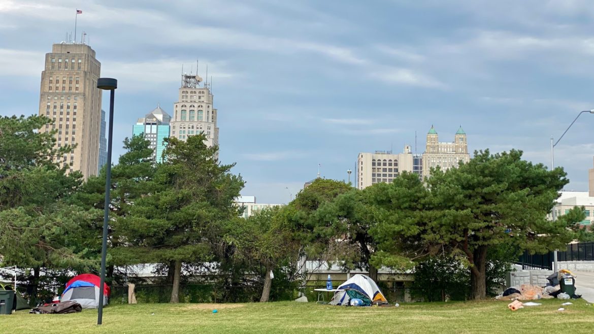 An encampment of houseless people near 10th and Harrison streets, with City Hall towering in the background.