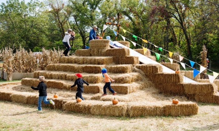 Kids playing on a large pyramid of hay. 