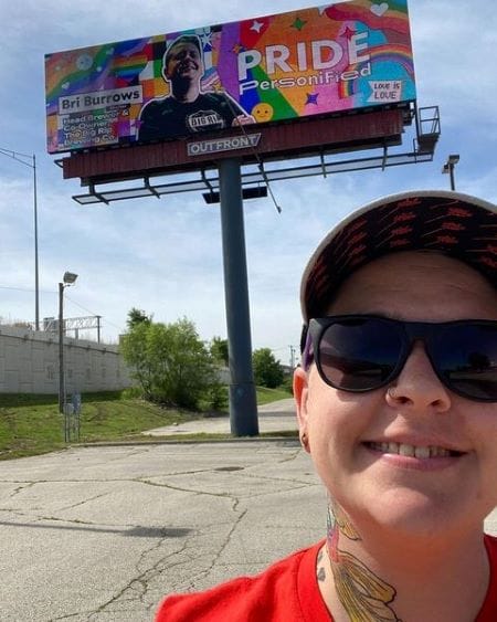 Big Rip Brewing Co. co-owner and head brewer Bri Burrows posing in front of Outfront Media’s “Pride Personified” billboard.