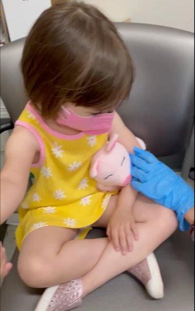 A four-year-old holds a plush piggy close as a nurse administers the COVID-19 vaccine.