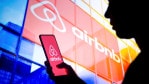 In this photo illustration, a woman's silhouette holds a smartphone with the Airbnb logo displayed on the screen and in the background.