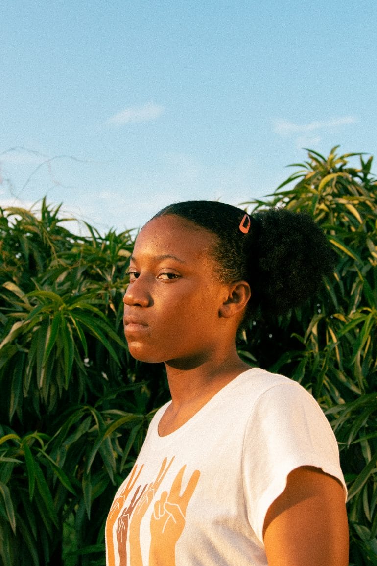 Liberty Williams looks directly into the camera lens, a young Black girl against a backdrop of lush greenery in Kansas City Community Garden. Liberty has attended Perkins’ class twice and has her own garden at home that she and her mom tend to. (Ji Stribling | Flatland)