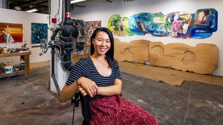 Artist Kathy Liao in her downtown studio with a draft (top right) of her artwork for the new KCI terminal. Titled, “Hello and Goodbye,” the piece will feature acrylic on birchwood panels and ceramic tiles.