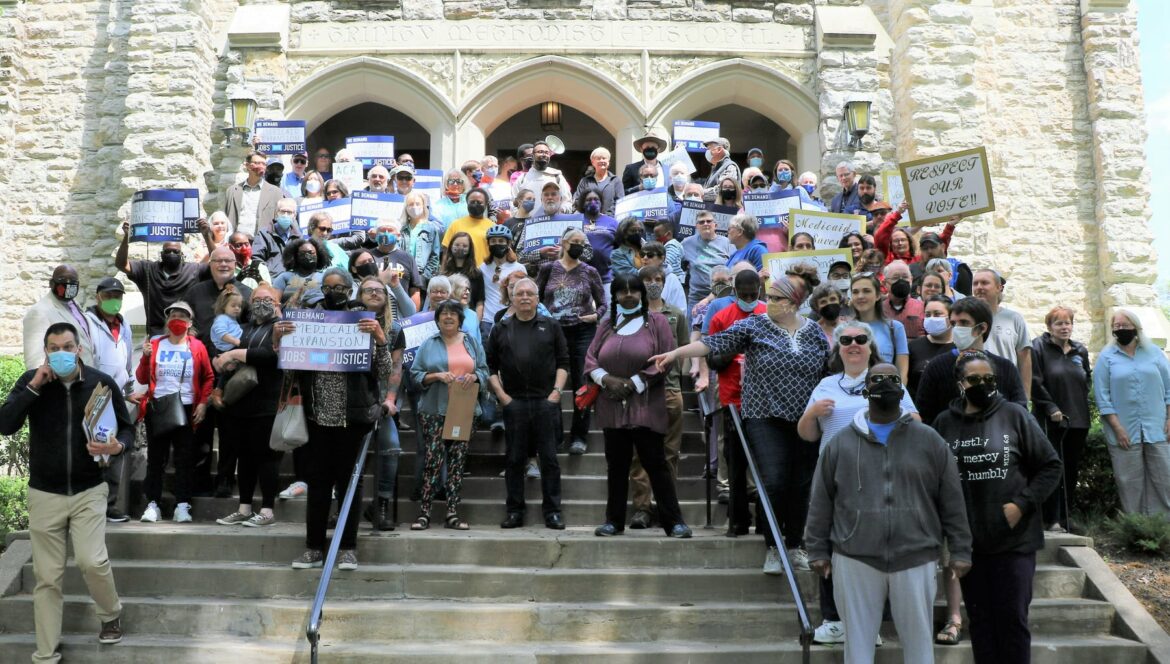 Group of people smile holding signs while standing on steps.