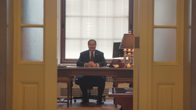 Man in a suit sits at a desk.