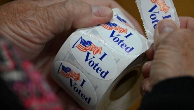 A poll worker peels off an "I Voted" sticker.