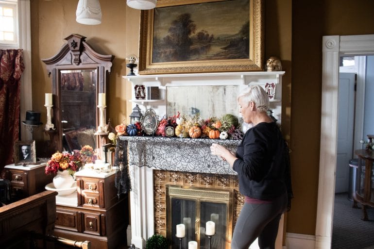 Woman stands in front of a fireplace with Halloween themed decor.