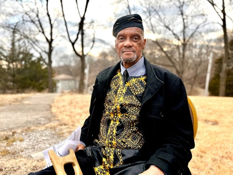 Parkville resident Archie J. Williams looks in the camera. Williams, wearing a black and gold garment on top of a pressed button down shirt and tie, holds papers that outline an agenda before his speech at the vigil for Washington Chapel. The church is a historic Black church in Parkville, Missouri that was recently broken into and a namesake stolen.