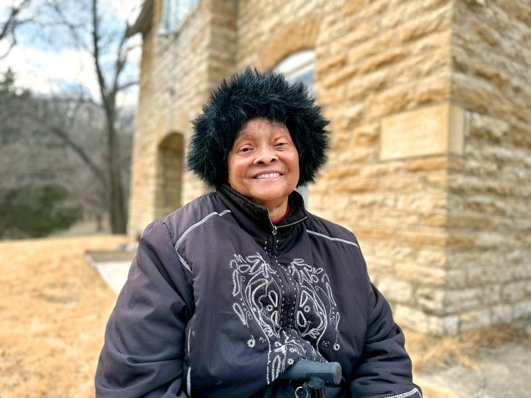 Pictured here is Cora Douglas, smiling into the camera, who is one of few congregants of Washington Chapel, a historic Black church in Parkville, Missouri. She has been one of the few dedicated members focused on revitalizing the chapel and ensure its history does not disappear. (photo by Vicky Diaz-Camacho for Flatland)