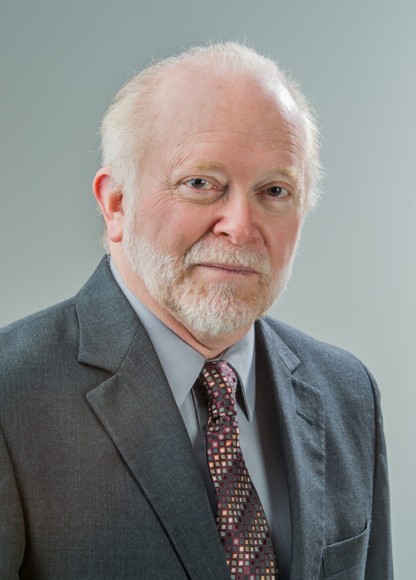 Headshot of older man in a suit with white hair and beard.