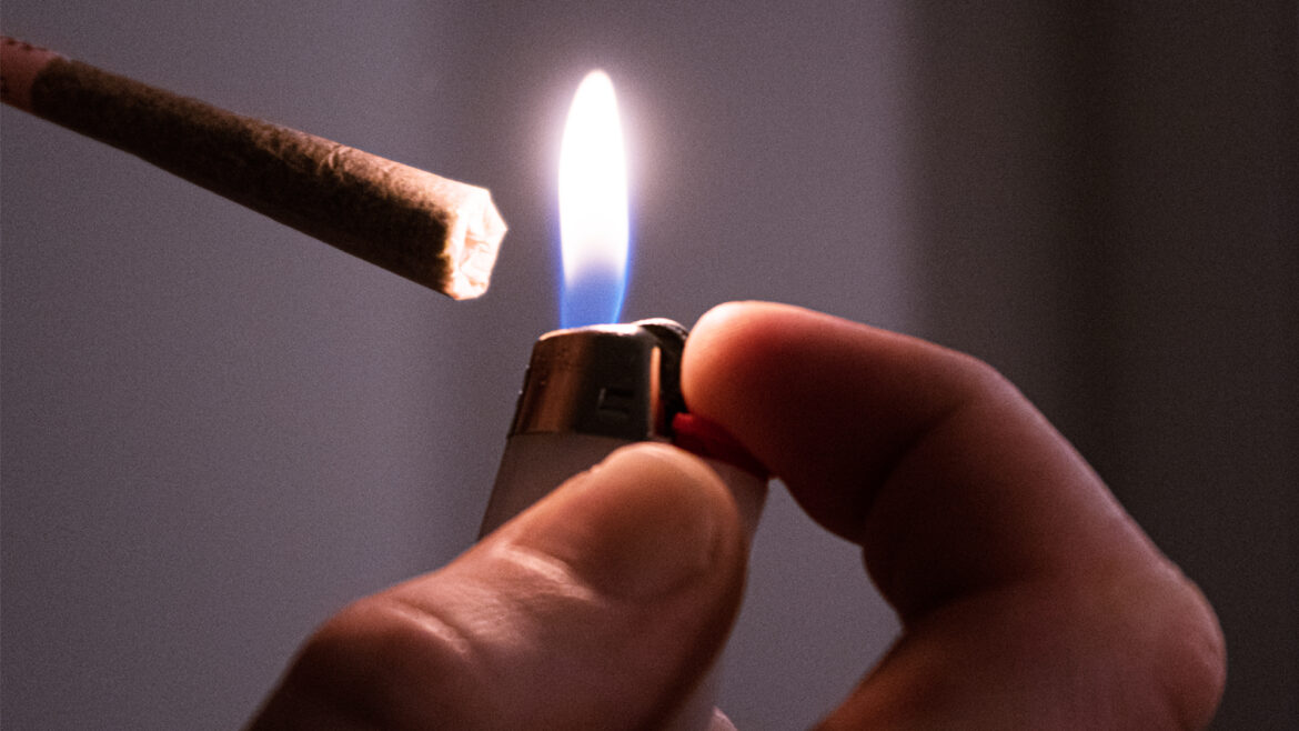 Close up of a hand holding a lighter up to the end of a joint.