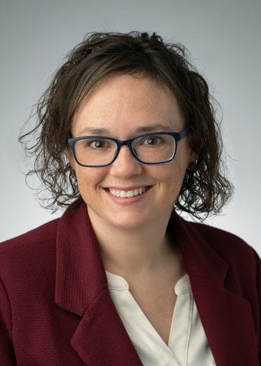A headshot of a woman with curly hair and glasses