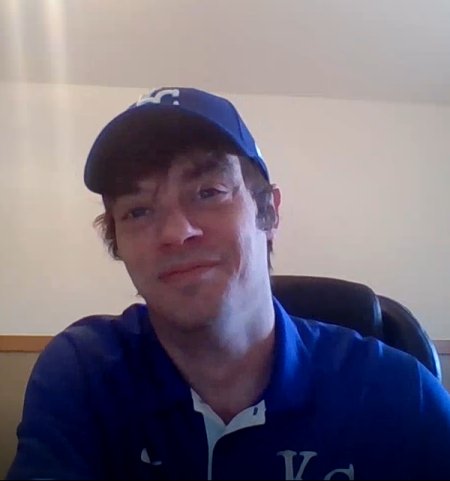 A man in a blue Royals polo and ball cap smiles.