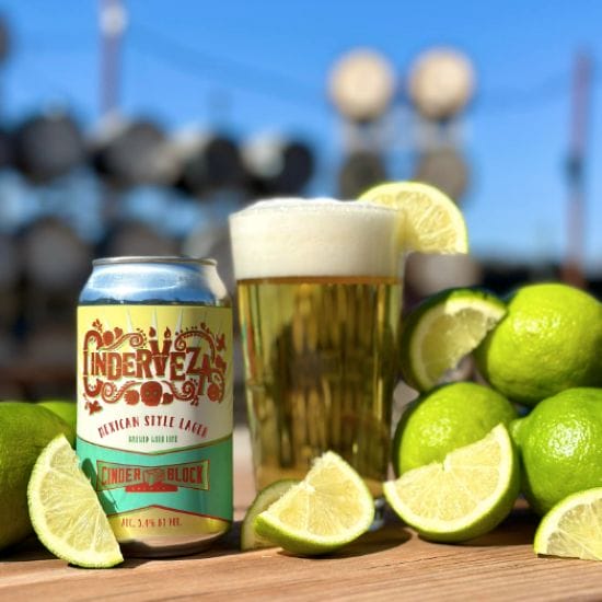 A can and a glass of Cinder Block Brewery's Cindervesa beer amid a pile of limes.