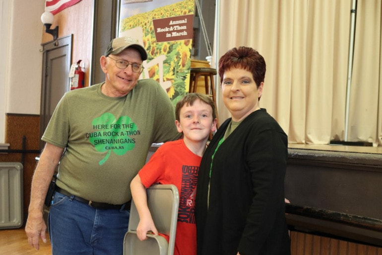 An older man in a hat stands next to a tween boy and a middle aged woman.