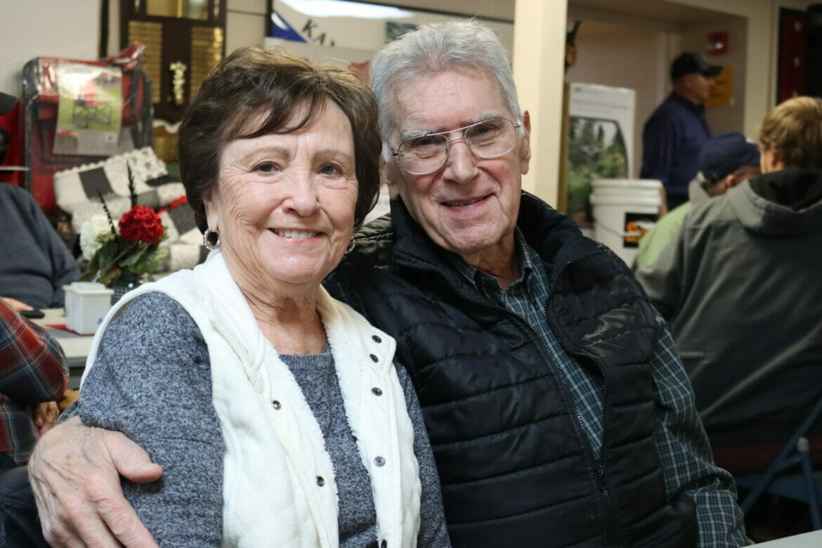 An older couple smile with their arms around one another.