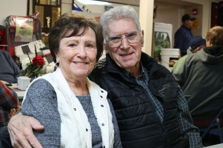 An older couple smile with their arms around one another.