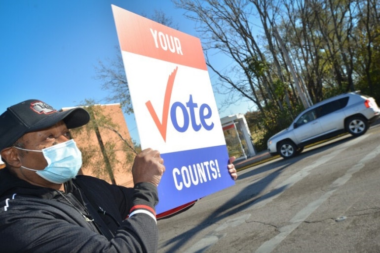 A man holds a "Your Vote Counts" sign.