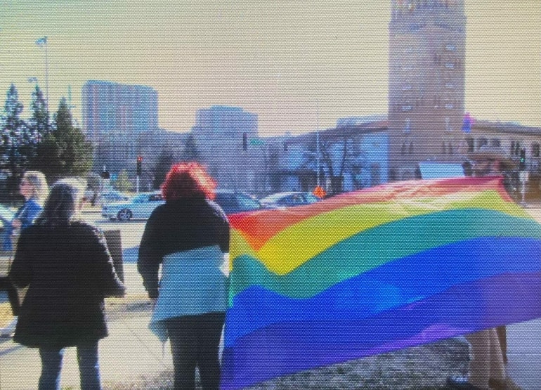 A woman stands beside a large multi-colored pride flag near the Country Club Plaza.