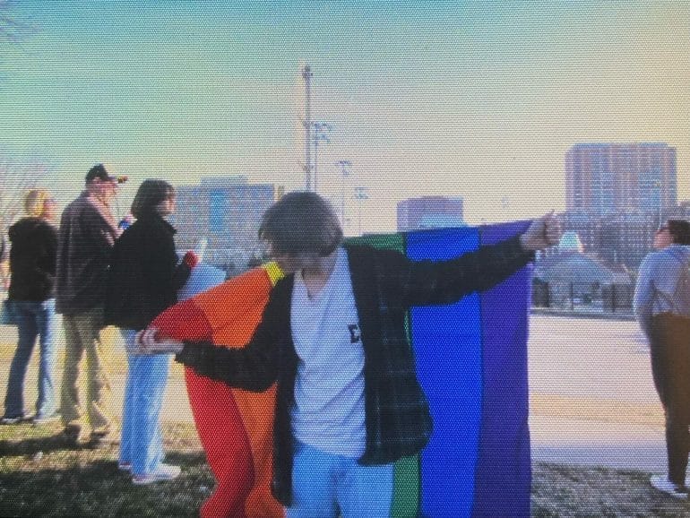A protest attendee holds a pride flag along their back, arms outstretched. They were attending a demonstration against SB134.