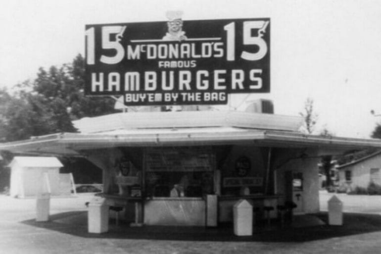 This 1948-era McDonald's restaurant tagline, "buy 'em by the bag," is unquestionably derivative of Walt Anderson's 1910s-era tagline, "sell 'em by the sack." McDonald's was originally started by the McDonald brothers in San Bernardino, California, in the 1940s.