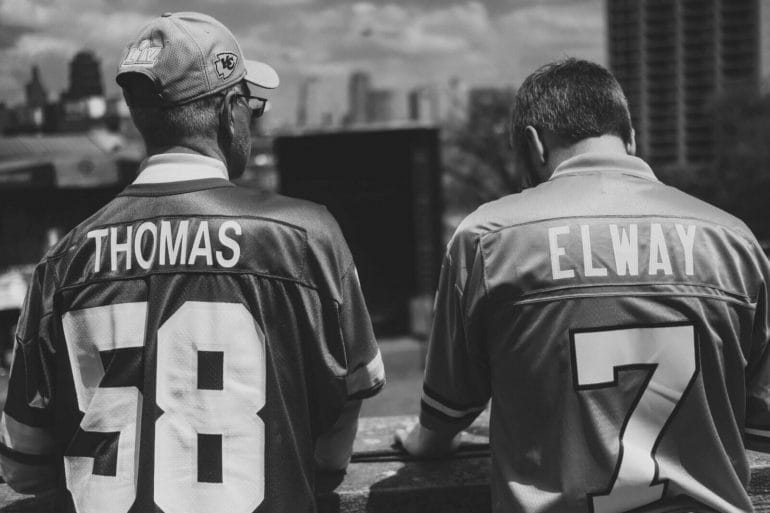 Fans in a Derrick Thomas jersey and a John Elway jersey share a moment at the NFL Draft.