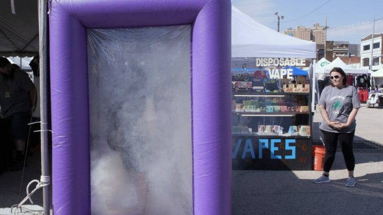A purple inflatable box fills with smoke while two people stand inside.