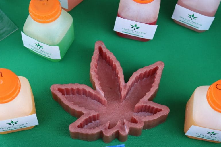 a cannabis leaf shaped ashtray is surrounded by little bottles of infused juice with a label that reads "League Treats"